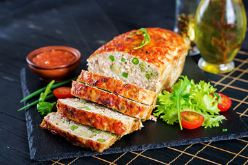 Tasty homemade ground  baked chicken meatloaf with green peas and broccoli on black table. Food american meat loaf.