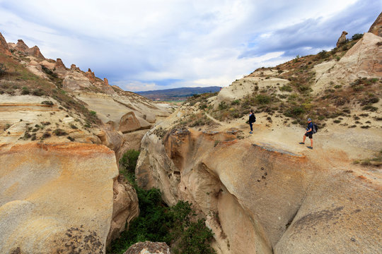 A young couple of tourists stands on the edge of a canyon in Cappadocia