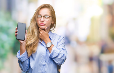 Young beautiful blonde business woman showing screen of smartphone over isolated background serious face thinking about question, very confused idea