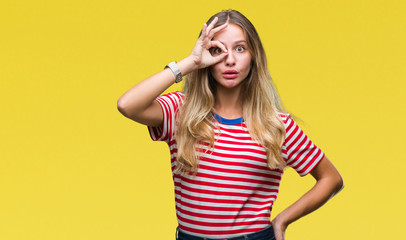 Young beautiful blonde woman over isolated background doing ok gesture shocked with surprised face, eye looking through fingers. Unbelieving expression.