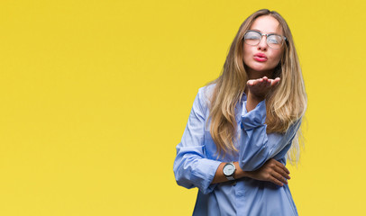 Young beautiful blonde business woman wearing glasses over isolated background looking at the camera blowing a kiss with hand on air being lovely and sexy. Love expression.