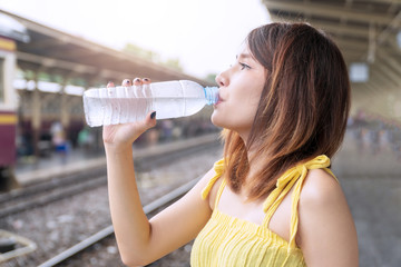 Traveler young woman drinking fresh water form bottles in her hands while waiting someone at train station. Lifestyle travel relax concept.