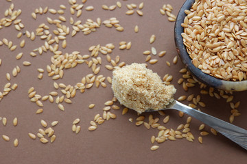 Ground white flax in a spoon, flax seeds on a brown background