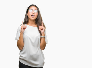 Young beautiful arab woman wearing glasses over isolated background amazed and surprised looking up and pointing with fingers and raised arms.