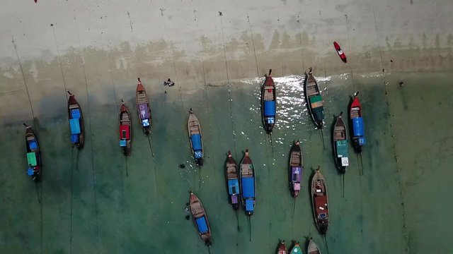 Aerial view top down pull up close up of the long tail boats, kayaks and people walking on the sand at Loh Dalum beach in Koh Phi Phi, Thailand. Drone 4K footage on a sunny day of a summer.