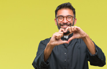 Adult hispanic catholic priest man over isolated background smiling in love showing heart symbol and shape with hands. Romantic concept.