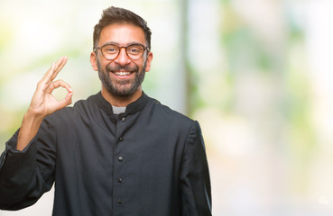 Adult hispanic catholic priest man over isolated background smiling positive doing ok sign with...