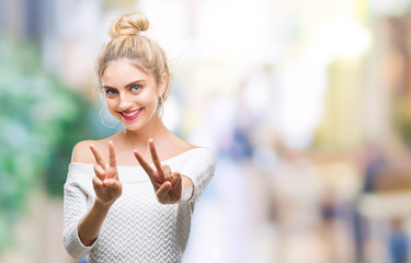 Young beautiful blonde and blue eyes woman over isolated background smiling looking to the camera showing fingers doing victory sign. Number two.