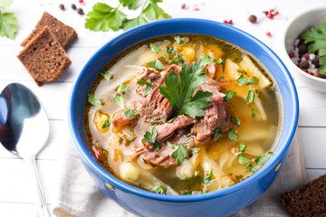 Russian traditional cabbage soup with meat and fresh herbs on a light table.