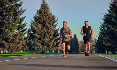 Fototapeta premium The old and young sportsmen running on the road