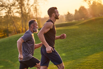 The two sportsmen running in the picturesque park on the sunset background