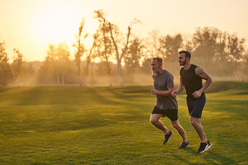 The two sportsmen running in the picturesque park on the sunset background