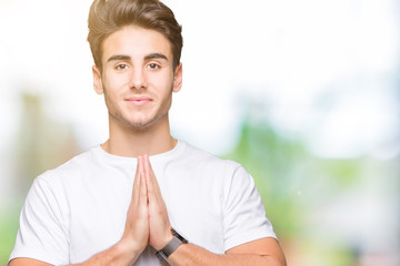 Young handsome man wearing white t-shirt over isolated background praying with hands together asking for forgiveness smiling confident.