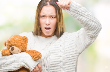 Young caucasian woman holding teddy bear over isolated background annoyed and frustrated shouting with anger, crazy and yelling with raised hand, anger concept