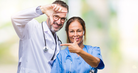 Middle age hispanic doctors partners couple wearing medical uniform over isolated background smiling making frame with hands and fingers with happy face. Creativity and photography concept.