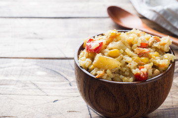Pilaf with vegetables and chicken in wooden bowl on wooden background. Copy space