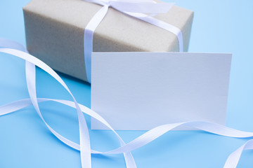 Brown gift box and white bow ribbon on blue background with paper card note for text
