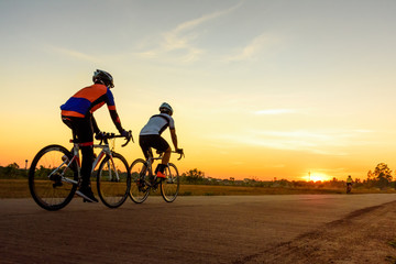 Fototapeta na wymiar Men ride bicycles on the road with beautiful colorful sunset sky. Sport and active life concept.