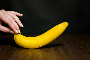 Banana with condom in girl hand. Dark background