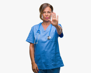 Middle age senior nurse doctor woman over isolated background doing stop sing with palm of the...
