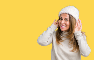 Beautiful middle age woman wearing winter sweater and hat over isolated background Trying to hear both hands on ear gesture, curious for gossip. Hearing problem, deaf