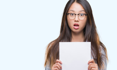 Naklejka premium Young asian woman holding blank paper over isolated background scared in shock with a surprise face, afraid and excited with fear expression
