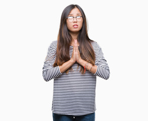 Young asian woman wearing glasses over isolated background begging and praying with hands together...