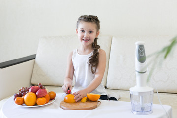 The child slices an orange with a knife. The girl cuts with a knife the fruit for making a cocktail.
