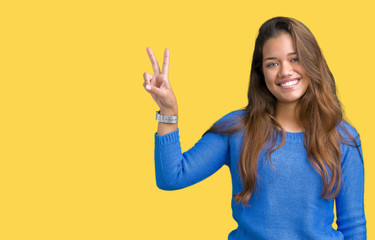 Young beautiful brunette woman wearing blue sweater over isolated background smiling with happy face winking at the camera doing victory sign. Number two.