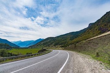Mountain road at sunset. Landscape with rocks, orange sunny sky with clouds and beautiful asphalt road in the evening in summer. Vintage toning. Travel background. Scenery with highway. Transportation