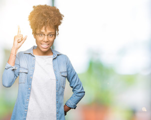 Beautiful young african american woman wearing glasses over isolated background pointing finger up with successful idea. Exited and happy. Number one.