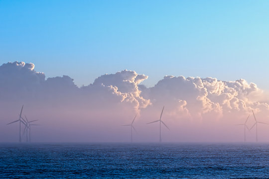 Clean energy. Misty morning wind turbines with low cloud bank at sea