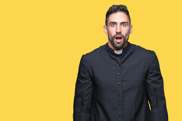 Young Christian priest over isolated background afraid and shocked with surprise expression, fear...