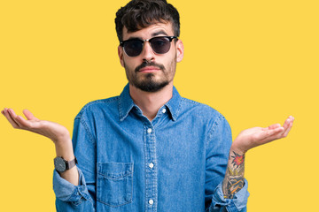 Young handsome man wearing sunglasses over isolated background clueless and confused expression...