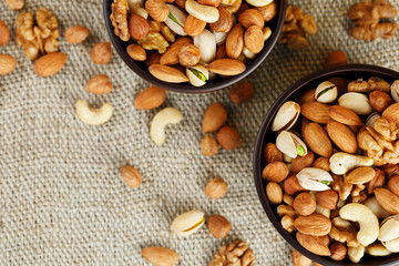 Mix of various nuts in a wooden cup against the background of fabric from burlap. Nuts as structure and background, macro. Top view.