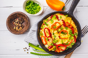 Traditional fritatta with peppers and potatoes in a cast iron pan. White wooden background.