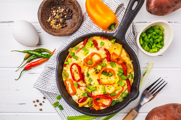 Traditional fritatta with peppers and potatoes in a cast iron pan. White wooden background.