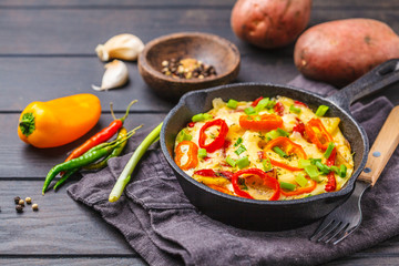 Traditional fritatta with peppers and potatoes in a cast iron pan. Dark wooden background