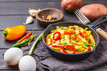 Traditional fritatta with peppers and potatoes in a cast iron pan. Dark wooden background