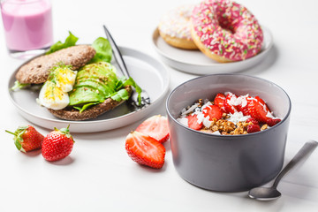 Beautiful breakfast: smoothie bowl, avocado toast and pink donuts on white background.