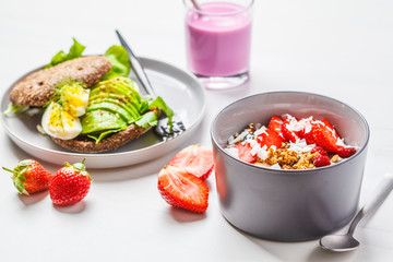 Strawberry smoothie bowl with granola, coconut, berries and avocado toast on a white background. Vegan breakfast.