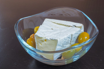 Camembert cheese with olives in a bowl on a black background