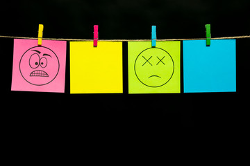 Copy space. Four stickers. On the pink page the expression of anger of smiley, on the yellow page shock. Stickers are attached to the rope with clothespins.