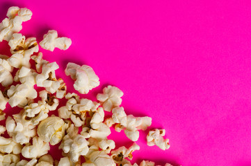 Fototapeta na wymiar Scattered cooked popcorn on pink background with copy space. Сoncept of leisure
