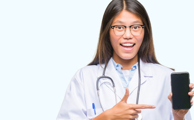 Young asian doctor woman holding smartphone over isolated background very happy pointing with hand and finger