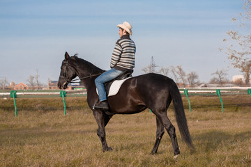 Man riding horse, striped pullover, blue jeans, hat, landscape