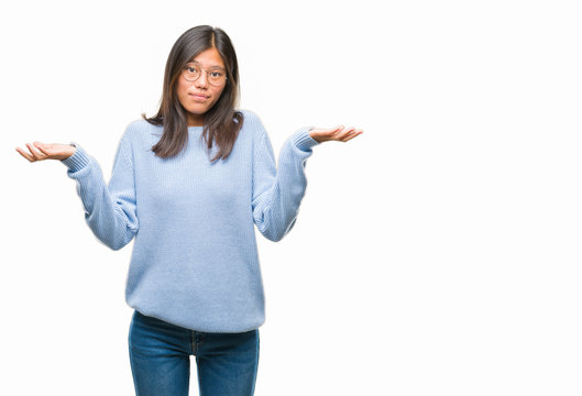 Young asian woman wearing winter sweater over isolated background clueless and confused expression with arms and hands raised. Doubt concept.