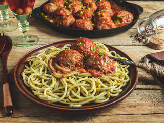 Homemade meatballs in tomato sauce with pasta on a plate. Frying pan on a wooden surface