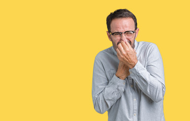 Handsome middle age elegant senior man wearing glasses over isolated background smelling something stinky and disgusting, intolerable smell, holding breath with fingers on nose. Bad smells concept.