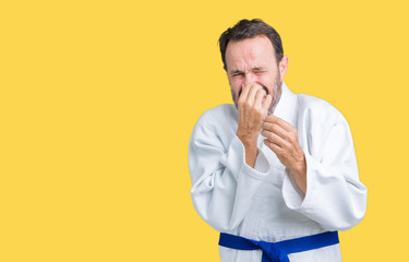 Handsome middle age senior man wearing kimono uniform over isolated background smelling something stinky and disgusting, intolerable smell, holding breath with fingers on nose. Bad smells concept.